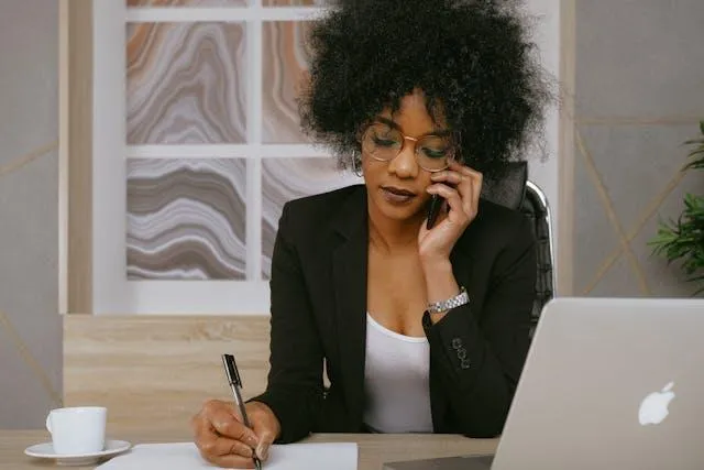 A woman taking a call and writing in her notepad in front of her laptop