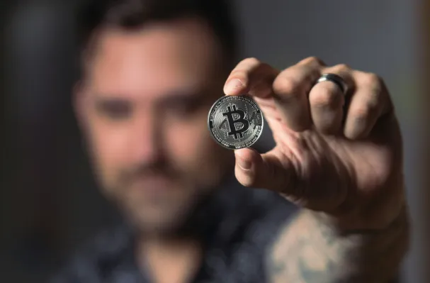 A man holding up a Bitcoin coin 